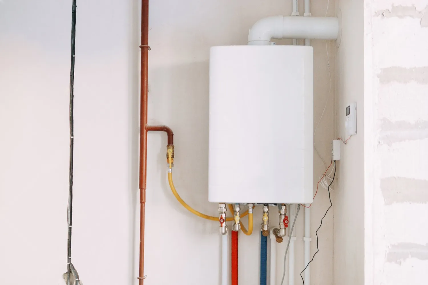 Installation of a gas boiler with colored pipes equipped with valves and connectors for efficient supply of hot and cold water in the residential water supply system